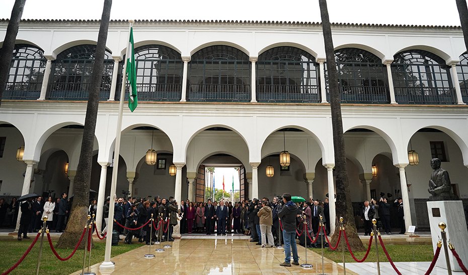 Juanma Moreno y Jesús Aguirre, junto al resto de autoridades, durante el acto de interpretación del himno e  izada de la bandera, en el Patrio del Recibimiento del Parlamento de Andalucía.